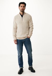 Beige pullover med halvdragkedja och ribbad textur; kombinerad med blå denimjeans och svarta chunky stövlar. Enkel, avslappnad outfit.