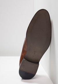 Semelle de chaussure en cuir marron avec surface texturée, présentant des clous en accent doré et un logo embossé. Taille 41 indiquée sur la semelle.