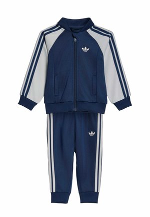 Børne træningssæt fra Adidas i marineblå og hvid med lynlåstrøje og bukser, der har mærkets tre-stribede design og trefoil-logo.