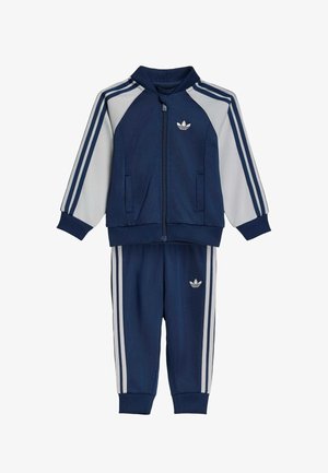 Donkerblauw-wit Adidas trainingspak voor kinderen, bestaande uit een jack met rits en een broek, uitgevoerd met het iconische drie-strepen ontwerp en het trefoil-logo van het merk.