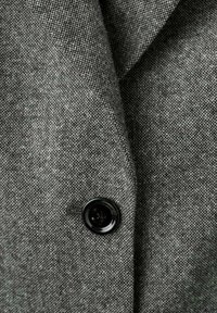 Tela gris texturizada de un blazer con un detalle de botón negro, que presenta un solapa de pico y un patrón sutil en toda su extensión.