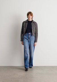 Giacca in tweed bianco e nero con un design aderente, abbinata a jeans blu a vita alta e scarpe nere. Texture morbide, silhouette moderna.