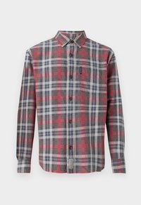 Chemise à carreaux dans des tons de gris, rouge et bleu. Manches longues, col pointu, poche avant et boutons foncés. Tissu texturé.