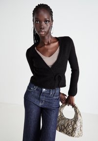 Svart, fuzzy omslagskardigan med knytning i livet, sammen med mørke denim vide bukser og en tekstureret slangeskins-design håndtaske.