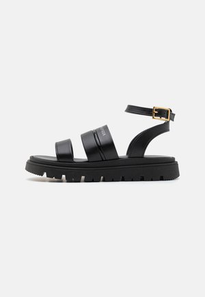 Black leather sandals with three wide straps, adjustable ankle buckle, and a textured black sole featuring a slight platform and ridges.