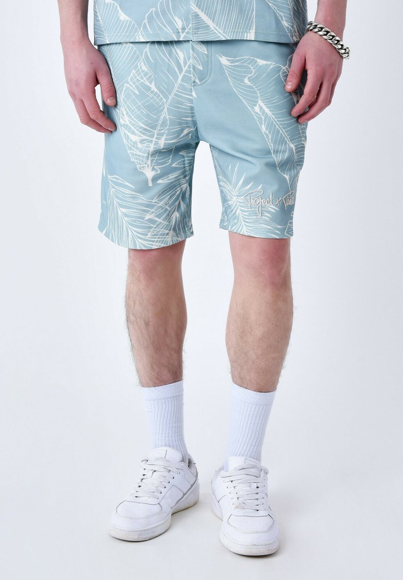 Pantalones cortos azul claro con patrones de hojas blancas, que presentan un corte relajado, una sutil marca y se combinan con zapatillas y calcetines blancos.