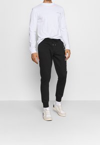 Zwarte joggingbroek met elastische boorden en een trekkoord in de taille, gecombineerd met een lange mouw wit shirt met een klein logo op de borst.