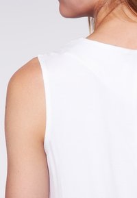 Top bianco senza maniche con una texture liscia e elastica. Il design presenta un collo rotondo, mettendo in risalto uno stile pulito e minimalista.