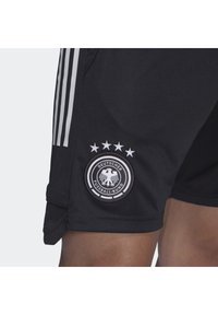 Czarne spodenki sportowe wykonane z teksturowanej tkaniny, z białymi paskami Adidas oraz haftowanym logo Niemieckiego Związku Piłki Nożnej z czterema gwiazdkami.