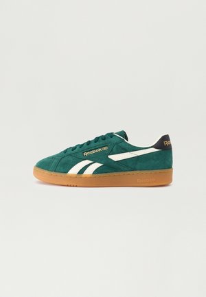Sneaker Reebok in camoscio verde con strisce bianche e suola in gomma, mostrata di lato su uno sfondo chiaro e uniforme.