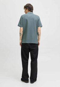 Groene katoenen polo met een gestructureerd oppervlak, korte mouwen en een kraag, gecombineerd met zwarte loszittende broeken en laarzen.