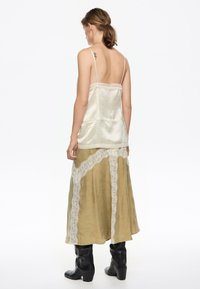 Camisola de seda crema con detalles de encaje, combinada con una falda de satén verde con detalles de encaje blanco, llevada con botas negras hasta la rodilla.