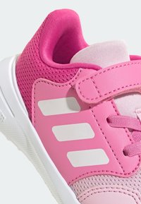 Chaussure de sport rose en mesh et cuir, avec des bandes blanches, une surface texturée et une bride Velcro. Design à bout arrondi.