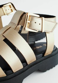 Guld, konstläder sandaler har en bred remdesign med en justerbar spänne, svart gummi sula och texturerade accenter.