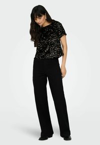 Haut noir à sequins avec une coupe décontractée et des manches courtes, associé à un pantalon noir taille haute à jambes larges et des bottines.