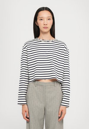 Chemise à manches longues raccourcie avec des rayures bleu marine et blanches, dotée d'un col texturé en perles. Associée à un pantalon léger à rayures fines gris.