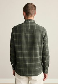 Camisa de botón de cuadros verdes hecha de tela suave, con dobladillo redondeado, mangas largas y patrones de cuadros blancos.