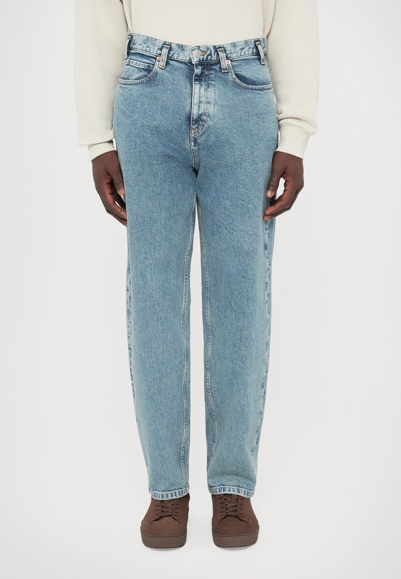 Τζιν παντελόνι σε ανοιχτό μπλε με χαλαρή γραμμή, �διαθέτει εμπρόσθιες τσέπες, κούμπωμα με κουμπιά και διακριτική φθορά. Συνδυασμένο με καφέ παπούτσια με κορδόνια.