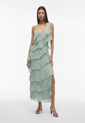 Hellgrünes, gestuftes Maxikleid mit Rüschenschichten, verstellbaren Spaghettiträgern und einem Seitenschlitz. Weicher, fließender Stoff mit transparenter Textur.