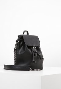 Czarny skórzany plecak z zapięciem na sznurek, klapką i paskiem ozdobionym łańcuszkiem. Gładka faktura i minimalistyczny design.