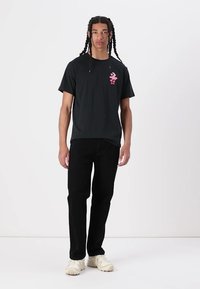 Sort t-shirt med et pink grafisk print, parret med sorte bukser og cremefarvede sneakers. Casual design, korte ærmer, afslappet pasform.