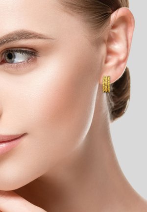 Orecchini a cerchio d'oro con tre bande sovrapposte, dotati di una finitura lucida e di delicate dettagliature testurizzate, indossati all'orecchio di un modello.
