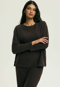 Brązowa bluzka z długim rękawem z miękkiej tkaniny, z okrągłym dekoltem, luźnym krojem i bocznymi rozcięciami, zestawiona z pasującymi spodniami.