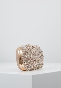 Sac à main en perles dans des tons métalliques dorés et beiges, présentant une surface texturée ornée de perles et de gemmes, de forme arrondie et avec une coque rigide.