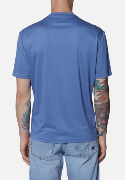 Maglietta blu a maniche corte realizzata in tessuto morbido, con colletto a girocollo e una superficie liscia. Tatuaggi visibili sulle braccia con design colorati.