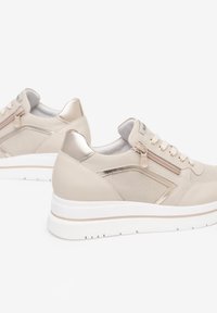 Beige sneakers met een textuur van mesh en een gladde leren afwerking. Voorzien van een zijrits, metalen accenten en een witte rubberen zool.
