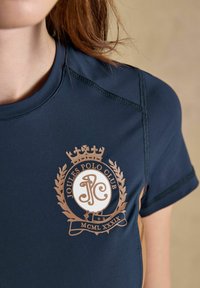 T-shirt bleu marine avec logo brun Joules Polo Club comprenant une couronne, une couronne de laurier et les chiffres romains MCML XXXIX sur la poitrine.