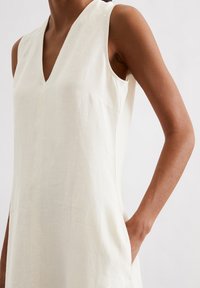 Ärmelloses, cremefarbenes Kleid aus leichtem Stoff. Verfügt über einen V-Ausschnitt, seitliche Taschen und ein sauberes, minimalistisches Design.