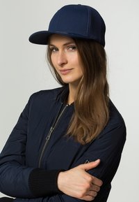 Navy blue cap made of soft fabric with a curved brim and mesh back. The model wears a matching bomber jacket with ribbed cuffs.