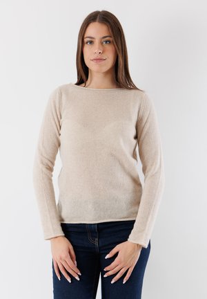 Pullover beige con maniche lunghe realizzato in un tessuto morbido, presenta un collo rotondo e un design leggermente aderente. Indossato con jeans blu scuro.