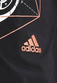 Camiseta de algodón negra con un gráfico geométrico en blanco y naranja y un logo de Adidas en naranja en la esquina inferior derecha.