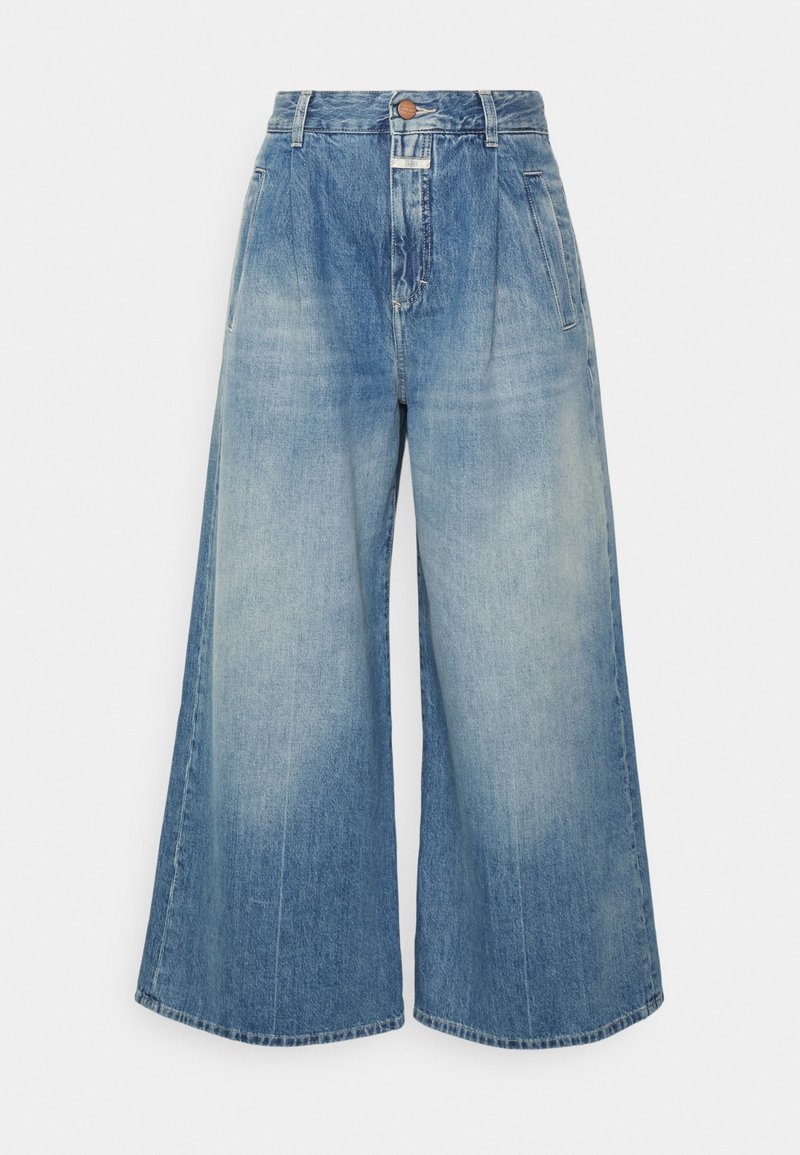 Jean en denim bleu à taille haute et jambes larges, avec bouton frontal, fermeture éclair et poches latérales, présentant des détails délavés.