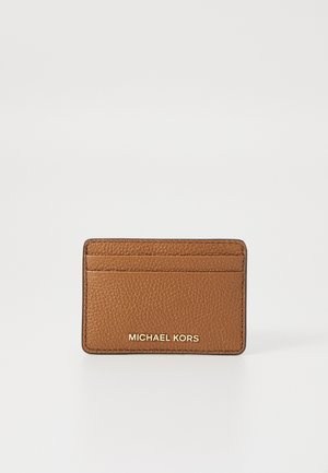 Brown leather card holder with a textured finish, four card slots, and a debossed "MICHAEL KORS" logo in gold. Minimalist design.