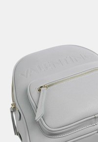 Zaino in pelle grigia con logo "Valentino" in rilievo, dettagli in cerniera dorata e design strutturato. Piccola tasca frontale per ulteriore spazio di archiviazione.