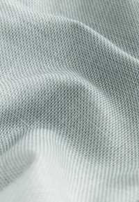 Close-up van lichtgrijze stof met een fijne, geweven structuur en zachte plooien die subtiele schaduwen en hooglichten creëren.