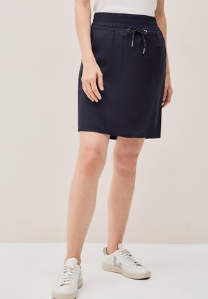 Gonna sportiva blu navy con cinturino elasticizzato e cordoncino. Tessuto liscio, lunghezza al ginocchio con tasche laterali. Indossata con sneakers bianche.