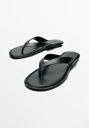 Sorte læder-tå-sandaler med flade såler, skrå remme og synlige syninger på hvid baggrund.