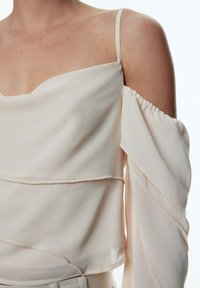 Hellbeige Bluse mit quadratischem Ausschnitt, durchsichtigen langen Ärmeln und geschichteter Textur. Hergestellt aus leichtem, fließendem Stoff.