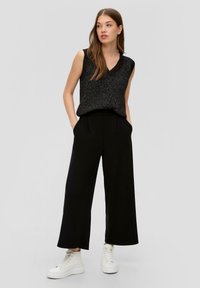 Pantaloni neri a gamba larga abbinati a un top senza maniche in maglia nera e argento, rifiniti con sneakers alte bianche. Texture liscia e vestibilità comoda.