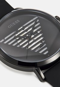 Black analog watch with a minimalist design. Features a transparent striped dial, black hands, and rubber strap. Logo displayed on the dial.