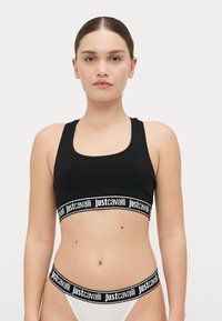 Soutien-gorge de sport noir avec large bande élastique portant le logo "justcavalli" en blanc. Texture lisse, décolleté en scoop et design dos nageur.
