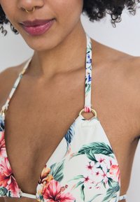 Bikini con motivo floreale, dotato di coppe triangolari, realizzato in tessuto bianco con dettagli rosa. Gli accessori in oro sulle spalline esaltano il design.