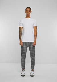 Weißes Rundhals-T-Shirt kombiniert mit grauen karrierten, taillierten Hosen. Sneakers mit schwarz-weißen Akzenten. Kurze Ärmel und lässiger Schnitt.