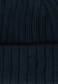 Beanie in maglia di colore blu navy scuro. Presenta una texture a coste verticali con una vestibilità aderente. Materiale morbido, simile alla lana.