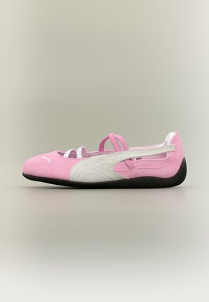Różowo-biały baletowy sneakers Puma z czarną podeszwą i krzyżującymi się elastycznymi paskami, widziany z boku na neutralnym tle.
