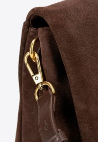 Brązowa zamszowa torebka wyposażona w złotą metalową zapięcie oraz brązowy skórzany pasek. Tekstura jest miękka, z widocznymi detalami szycia.